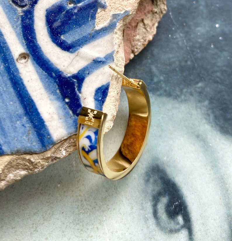 Op de afbeelding: Gouden creolen met een blauw en wit patroon. De oorbellen zijn van metaal en hebben een scharnier sluiting.