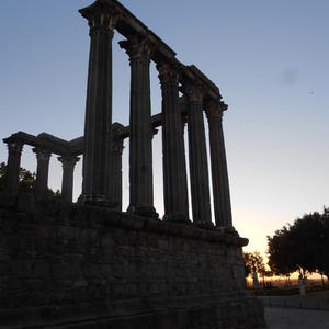 Op de afbeelding: Silhouet van Romeinse ru&iuml;nes tegen een schemerige lucht. De oude stenen kolommen staan hoog, wat een dramatisch tafereel cre&euml;ert.