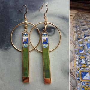 May include: Gold hoop earrings with green and blue tile-patterned pendants. The tiles have a white background with blue and yellow geometric designs.