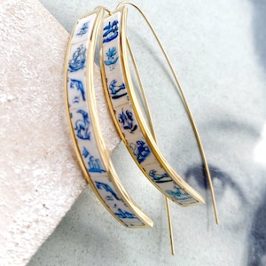 Op de afbeelding: Een paar gouden creolen met een blauw en wit patroon. Het patroon bevat verschillende kleine afbeeldingen, waaronder bloemen, vogels en geometrische vormen.