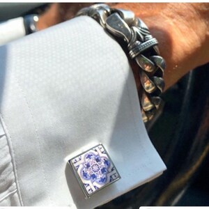 May include: A pair of silver cufflinks with a blue and white patterned design. The cufflinks are square shaped and have a silver border.