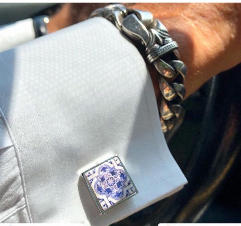 May include: A pair of silver cufflinks with a blue and white patterned design. The cufflinks are square shaped and have a silver border.