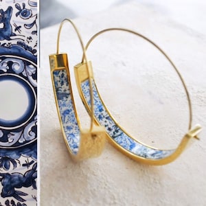 Könnte beinhalten: Ein Paar goldene Creolen mit einem blauen und weißen Muster. Das Muster erinnert an traditionelle Delftware-Keramik.