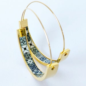 Può includere: Orecchini a cerchio dorati con un designo a motivi bianchi e blu. Il motivo ricorda le piastrelle tradizionali.