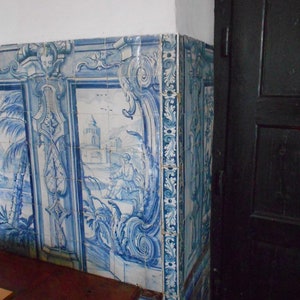 Peut inclure: Des carreaux bleus et blancs &agrave; motifs floraux et une sc&egrave;ne repr&eacute;sentant un b&acirc;timent et des palmiers. Les carreaux sont dispos&eacute;s verticalement et sont plac&eacute;s contre un mur blanc.