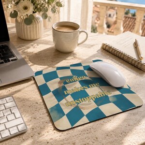 Peut inclure: Un tapis de souris carré avec un motif à carreaux bleu et crème, un graphique de tache de café et le texte coffee makes me unstoppable en lettres jaunes. Le tapis de souris est placé sur une surface de bureau à côté d'une souris d'ordinateur.