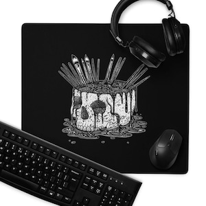 May include: Black mousepad with a skull design, paintbrushes, and a keyboard. The skull is white with black shading and dripping liquid. Black headphones and a mouse are also visible.