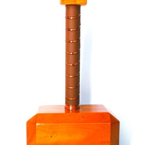 May include: A wooden hammer with a rectangular head and a cylindrical handle wrapped in brown leather. The handle is accented with copper-coloured bands. The top of the hammer is a smaller, rectangular piece of wood. The hammer is a light brown colour.