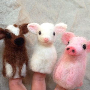 Pode incluir: Tr&ecirc;s fantoches de dedo feitos &agrave; m&atilde;o: uma vaca marrom e branca, um cordeiro branco e um porco rosa. Cada fantoche &eacute; feito de um material macio e texturizado, com tra&ccedil;os faciais detalhados e orelhas pequenas e eretas.