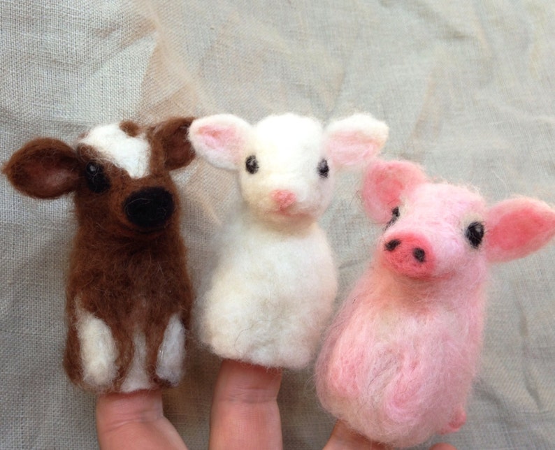 Pode incluir: Tr&ecirc;s fantoches de dedo feitos &agrave; m&atilde;o: uma vaca marrom e branca, um cordeiro branco e um porco rosa. Cada fantoche &eacute; feito de um material macio e texturizado, com tra&ccedil;os faciais detalhados e orelhas pequenas e eretas.
