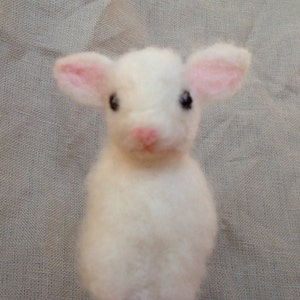 Pode incluir: Uma figura de cordeiro feita &agrave; m&atilde;o em feltro branco com o interior das orelhas e o nariz rosa. O cordeiro tem olhos pretos e uma apar&ecirc;ncia fofa e texturizada. A figura &eacute; um item artesanal charmoso.