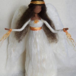 May include: A white felt angel doll with brown hair, a gold headband, and a white dress with a gold sash. The angel has white wings and is holding golden strands in each hand.