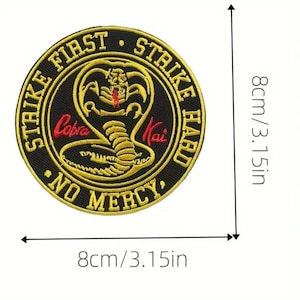 Peut inclure: Un écusson brodé noir et jaune avec un cobra et le texte "Strike First Strike Hard No Mercy" et "Cobra Kai". L'écusson mesure 8 cm de diamètre.
