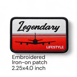 Puede incluir: Parche bordado termoadhesivo con borde negro. El parche presenta un fondo rojo y blanco con una silueta de avión negra. La palabra "Legendary" está en escritura negra encima del avión, y "LIFESTYLE" debajo. Mide 5,7 x 10,2 cm.