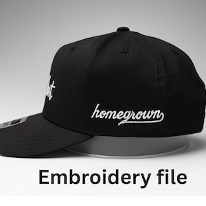 Pode incluir: Boné de beisebol preto com texto bordado branco que diz "hustle" e "homegrown". O boné tem uma aba curva e um botão na parte superior. As palavras "Embroidery file" são impressas abaixo.