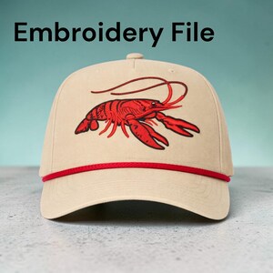 May include: A tan baseball cap with a red embroidered lobster design on the front. The cap has a red rope detail along the brim and the text "Embroidery File" at the top.