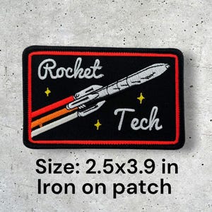 May include: Black iron-on patch with a white rocket ship and the text "Rocket Tech" in white. The patch is 2.5 inches by 3.9 inches.