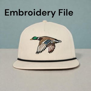 May include: Cream-colored baseball cap with a black rope detail and a detailed embroidered image of a flying duck. The duck features green, brown, blue, and white colors. The text "Embroidery File" is above the cap.