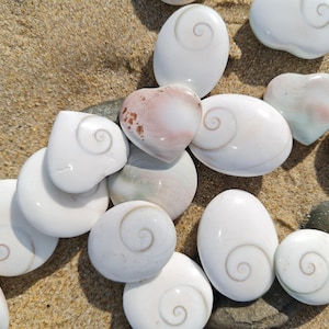 Peut inclure: Un ensemble de pierres blanches polies avec un motif en spirale, dont certaines en forme de cœur, disposées sur du sable. Les pierres sont de tailles variées et ont une surface lisse et brillante. Certaines pierres présentent des teintes roses et brunes.