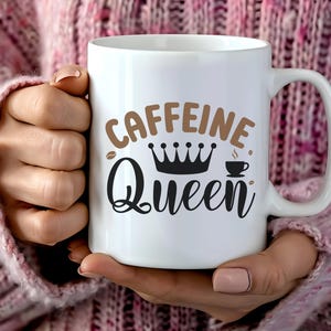 May include: White ceramic coffee mug with the words "CAFFEINE Queen" in brown and black lettering. The design includes a coffee bean, a crown, and a small coffee cup. The mug has a large handle.