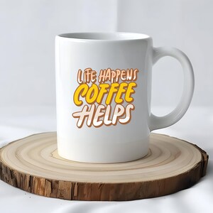 Op de afbeelding: Een witte keramische koffiemok met de tekst "LIFE HAPPENS COFFEE HELPS" in een geel en bruin ontwerp. De mok staat op een ronde, houten onderzetter met een natuurlijke rand. De achtergrond is neutraal van kleur.