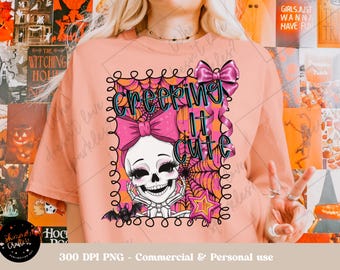Puede incluir: Camiseta color melocotón con un gráfico temático de Halloween. El diseño presenta una calavera sonriente con un lazo rosa, telarañas y la frase "CREEPING IT CUTE" en turquesa y rosa. Un murciélago y una estrella completan el diseño.