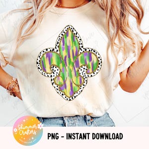 Może przedstawiać: Kremowa koszulka z motywem fleur-de-lis. Fleur-de-lis jest wypełniony zielonymi, żółtymi i fioletowymi pociągnięciami pędzla, obrysowanymi złotym brokatem i czarno-białą obwódką w kropki. Tekst "PNG - INSTANT DOWNLOAD" znajduje się na dole.