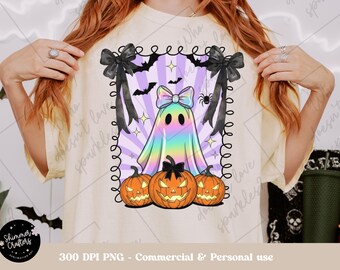 May include: A cream-colored t-shirt featuring a Halloween-themed graphic. The design includes a rainbow-colored ghost with a bow, three jack-o'-lanterns, bats, and a spider. The graphic is framed with black bows and a decorative border.