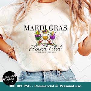May include: Cream-colored t-shirt featuring the words "Mardi Gras Social Club" with three wine glasses in purple, yellow, and green, each with a festive hat. The phrase "Let the Good Times Roll" is below the club name.