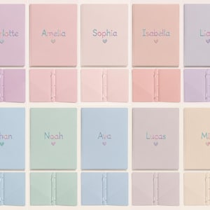 May include: A collection of ten pastel-colored notebooks, each featuring a personalized name embroidered in colorful thread above a small heart icon. The notebooks are displayed in two rows, showing both the front covers and the open interior spines.