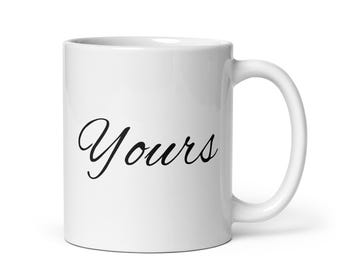 May include: White ceramic mug with a curved handle. The word "Yours" is written in a black, elegant script across the front of the mug. The mug is designed for hot or cold beverages.