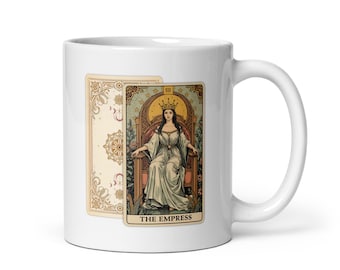 May include: White ceramic mug featuring a tarot card design. The card depicts "The Empress" in a flowing gown, seated on a throne. The mug also shows a decorative card back. The design is in shades of beige, gold, and green.