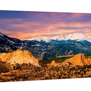Puede incluir: Impresi&oacute;n panor&aacute;mica en lienzo de un paisaje monta&ntilde;oso al atardecer. La imagen presenta monta&ntilde;as nevadas, formaciones rocosas anaranjadas y un cielo colorido con tonos de azul, naranja y rosa. La obra de arte est&aacute; estirada sobre un marco de madera.
