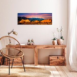 Puede incluir: Impresi&oacute;n de arte de paisaje panor&aacute;mico que presenta una cordillera con picos nevados bajo un cielo vibrante al atardecer. El primer plano muestra formaciones rocosas doradas. Una pieza decorativa para el hogar o la oficina.