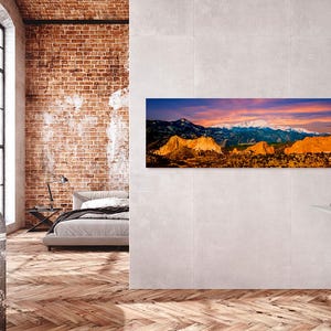 Puede incluir: Una fotograf&iacute;a panor&aacute;mica de un paisaje monta&ntilde;oso con picos nevados bajo un cielo vibrante al atardecer. La obra de arte se exhibe en un ba&ntilde;o moderno, sobre un tocador con un espejo redondo y un lavabo blanco.