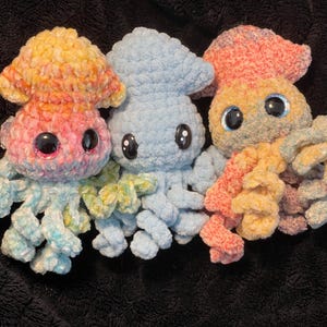 Könnte beinhalten: Drei gehäkelte Octopus-Plüschtiere in verschiedenen Farben. Der Octopus links ist rosa und gelb, der mittlere Octopus ist blau und der Octopus rechts ist orange und gelb.