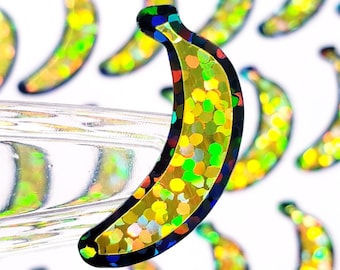May include: A close-up of a glittery gold banana sticker with a black outline. The sticker is iridescent and has a holographic finish.