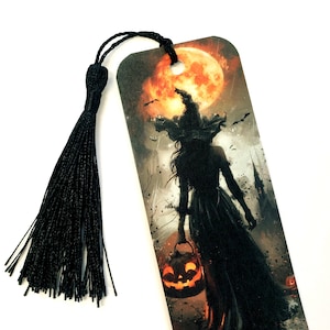 May include: A Halloween-themed bookmark featuring a witch silhouette against a full moon. The witch is holding a jack-o'-lantern. A black tassel is attached to the top of the bookmark. The background includes bats and a spooky castle.