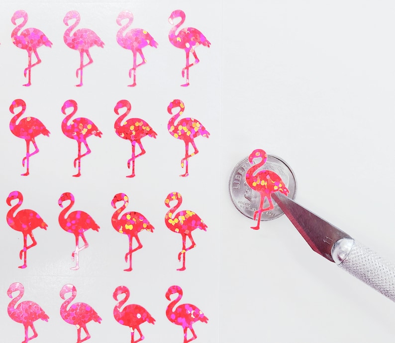 May include: Sheet of pink and red glitter flamingo stickers. The stickers vary in shades of pink and red, with some featuring yellow glitter accents. A small sticker is being cut with a craft knife.