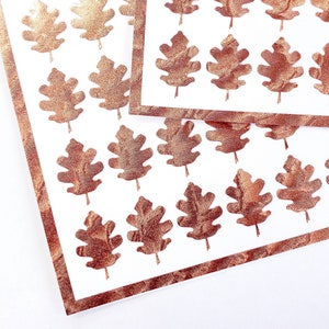 May include: A sheet of white paper with a gold border and a pattern of copper-colored oak leaves.