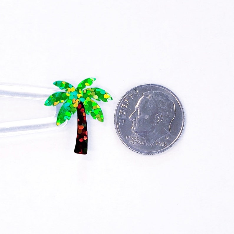 Op de afbeelding: Een groene en iriserende glitter palmboom uitsnijding, ongeveer de grootte van een Nederlandse tien cent munt.