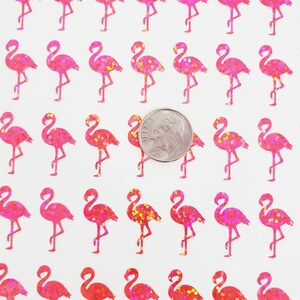 May include: Sheet of pink glitter flamingo stickers. Each flamingo is standing on one leg with its neck curved. A dime is included for size reference. The stickers have a glittery texture and are on a white background.