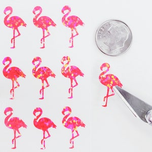 May include: Sheet of pink flamingo stickers with glitter accents. A dime is next to the stickers for size comparison. A craft knife is cutting one of the stickers. The stickers are on a white background.