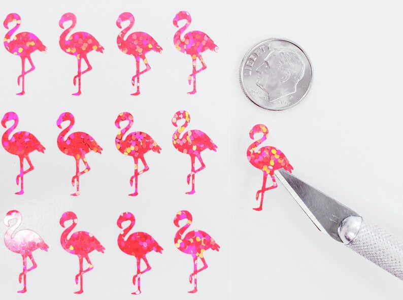 May include: Sheet of pink flamingo stickers with glitter accents. A dime is next to the stickers for size comparison. A craft knife is cutting one of the stickers. The stickers are on a white background.