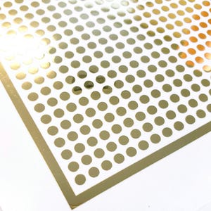 May include: A sheet of gold adhesive dots on a white background. The dots are arranged in a grid pattern.