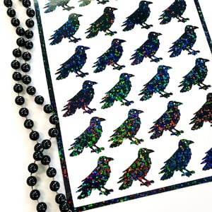 May include: A sheet of iridescent raven stickers. The ravens are black with a rainbow glitter finish.