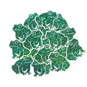 May include: A collection of green glitter frog stickers with white outlines. The stickers are in various poses, with a shiny, textured appearance. The frogs are clustered together against a white background.