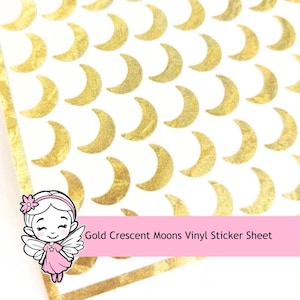 May include: A vinyl sticker sheet featuring a repeating pattern of metallic gold crescent moons on a white background. A small cartoon character with wings and a pink dress is positioned in the corner with the text Gold Crescent Moons Vinyl Sticker Sheet.