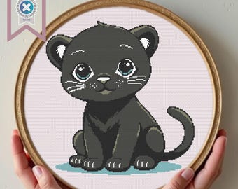 Può includere: Schema di punto croce di un cucciolo di pantera nera con occhi azzurri seduto su uno sfondo bianco.