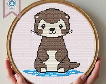Può includere: Uno schema di punto croce di una lontra marrone e bianca seduta su un disegno di acqua blu e bianco. La lontra ha un viso da cartone animato carino con occhi grandi e un piccolo sorriso.